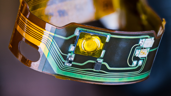 Closeup of ribbon cable with green and yellow copper lines on flexible PCB from headphones