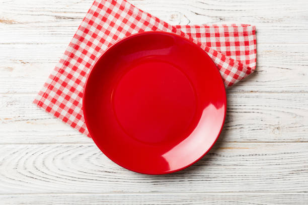 Top view on colored background empty round red plate on tablecloth for food. Empty dish on napkin with space for your design