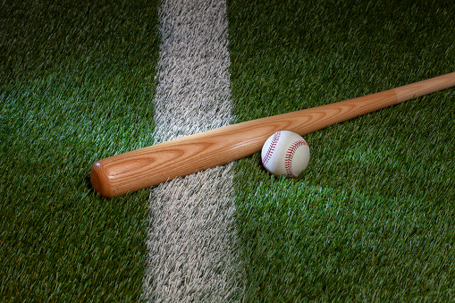Baseball and bat on grass field with white stripe