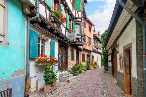 A charming and colorful narrow cobblestone alley in the medieval town of Eguisheim, France, in the Alsace region of Eastern France, along the Alsatian wine route. Eguisheim is a commune in the Haut-Rhin department in Grand Est in north-eastern France and is considered one of the most beautiful villages in France.