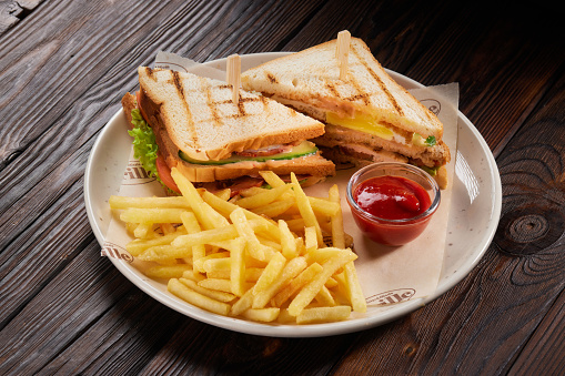 Two sandwiches with french fries and ketchup on white plate on wooden table. Fast food. Horizontal composition