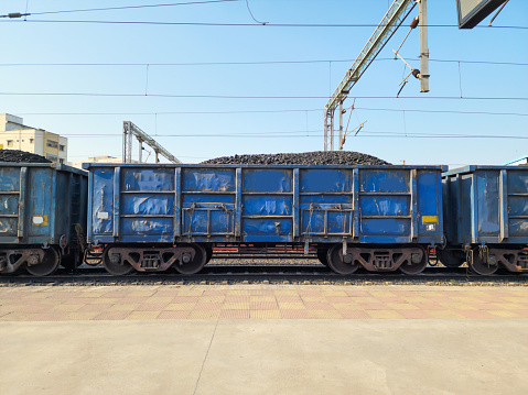 Stock photo of blue color painted open goods wagon loaded with charcoal transported to power, metal, Chemical production.Picture captured under bright sunlight at Hyderabad, Telangana, India.