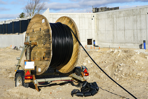 A trailer with a large spool of wooden black high voltage power cable at the construction site of a new large industrial facility