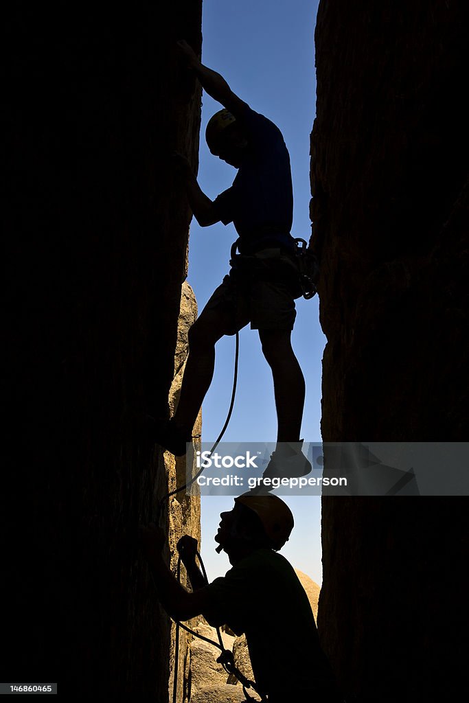Team of rock climbers. A team of rock climbers are silhouetted as they work their way up a chimney in Joshua Tree National Park. Achievement Stock Photo