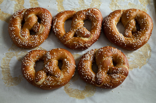 Soft, hot, salted pretzels on stained parchment showing just baked from the oven
