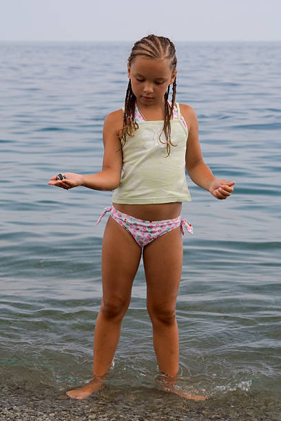 a little girl stands in water ashore exterminating and gets on the hip stone