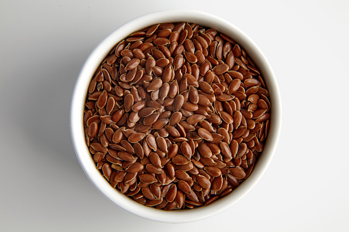 Flax seeds in a white ceramic bowl on a white background.
