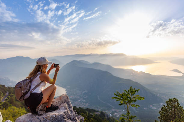 A happy girl with a backpack photographs the seascapes of Montenegro from the top of the mountain stock photo
