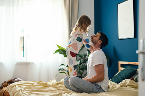 Unrecognizable daughter and father in sleepwear playing together in the bed.