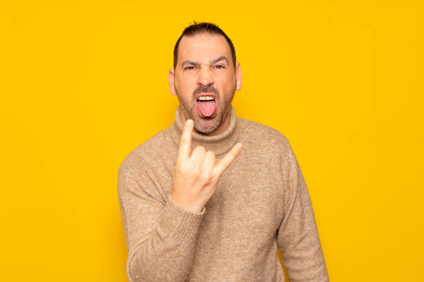 istock Bearded hispanic man wearing turtleneck isolated over yellow background showing rock gesture with fingers and sticking out tongue. Concept of rebellion and anarchism. 1468618391