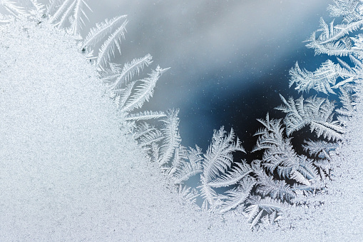 Frost pattern on glass over blurred blue background, macro photo, natural winter backdrop