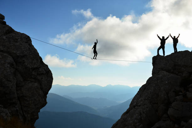 walking on a tightrope and a successful team in the mountains stock photo