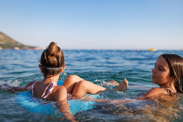 Two sisters in bathing suits play with an inflatable ring in the sea stock photo
