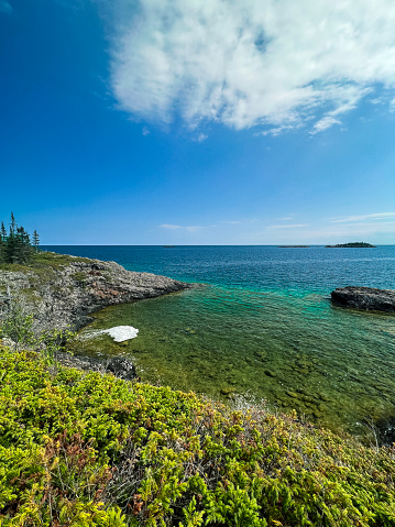 Looking out over the vast expanse and pure waters of Lake Superior from the coast of Isle Royale National Park. A rocky stone basin is in the forefront of view. Small islands covered in green evergreen trees can be seen in the distance. Located in the Upper Peninsula of Michigan.