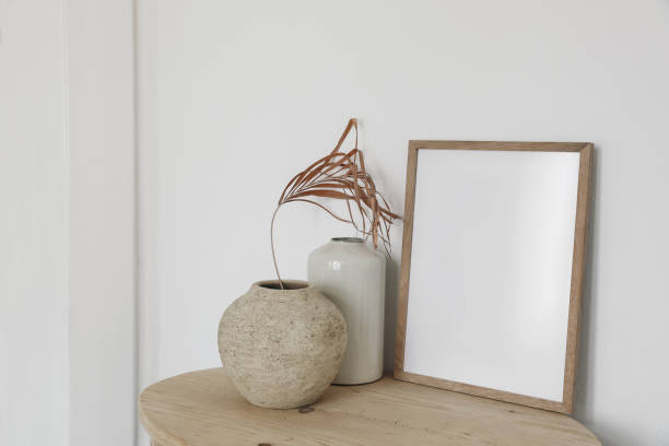 istock Blank wooden picture frame mockup on old round console table. Dry palm leaf in textured vase. White wall background. Empty copyspace. Elegant boho interior. Living room, artistic atelier display. 1468645527
