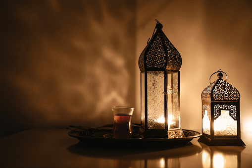 Arabic lantern glowing at night. Dark background, ornamental golden shadows. Festive greeting card, invitation. Muslim holy month Ramadan Kareem, Turkish tea. Eid ul Fitr, Eid ad Adha. Iftar dinner.