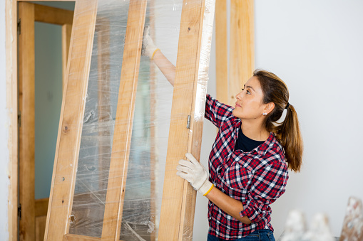 Latin woman carrying wooden door during renovation works in new apartment.