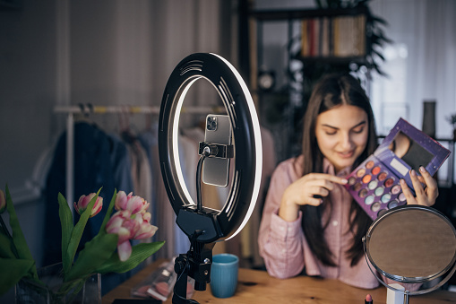 One woman, young female influencer giving make up tutorial, she is filming herself with smart phone.