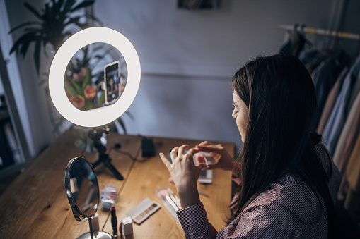 One woman, young female influencer giving make up tutorial, she is filming herself with smart phone.