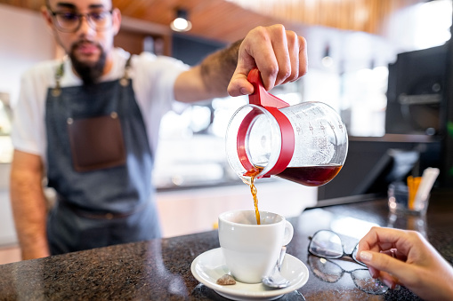 Male barista pouring coffee into the cup of customer at cafe counter