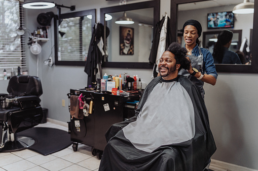 A black man who is getting his hair braided smiles while talking with his female hair dresser.