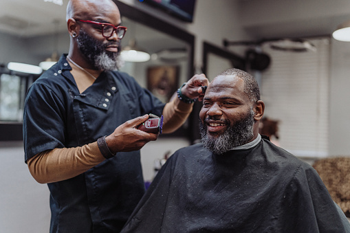 Mature adult black man smiles while having his hair cut at the barber shop.