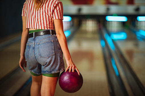 A girl in denim shorts is holding a bowling ball