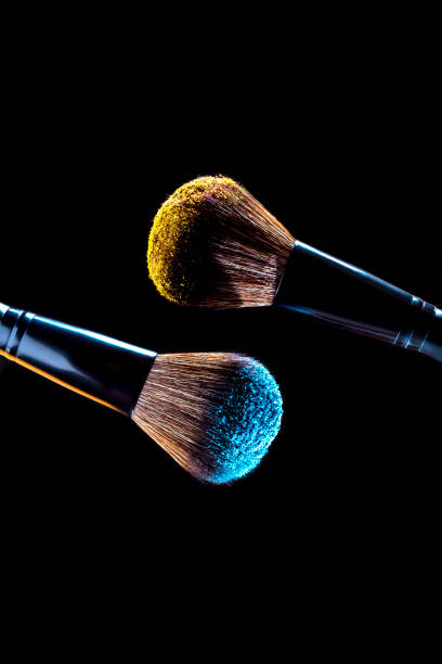istock Cosmetics makeup brushes with yellow and blue colored powder on a dark background 1468660052