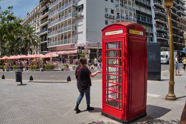 buenos aires, argentina - 28 October 2022: a woman is walking on the square next to the Recoleta cemetery and passes a typical red british phone booth