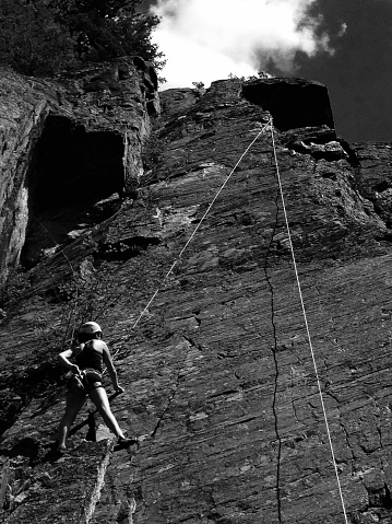 Black and white still of a rock climber plotting her course up a rock face