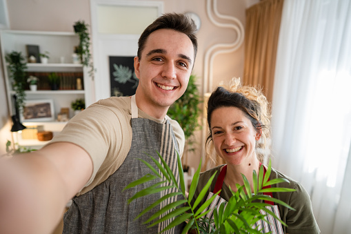 Couple caucasian man and woman wife and husband planting flowers together taking care of home plants real people domestic life family gardening concept take selfie photo with smartphone UGC