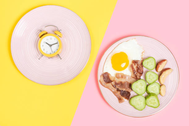 Plate with food and empty plate on pink and yellow background top view, intermittent fasting concept. stock photo
