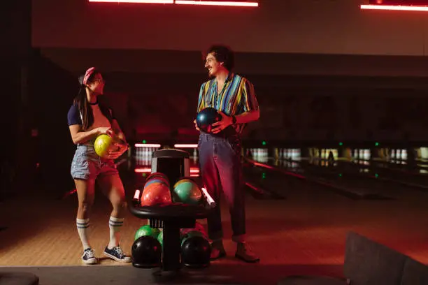 Multiracial couple looking at each other while holding bowling balls
