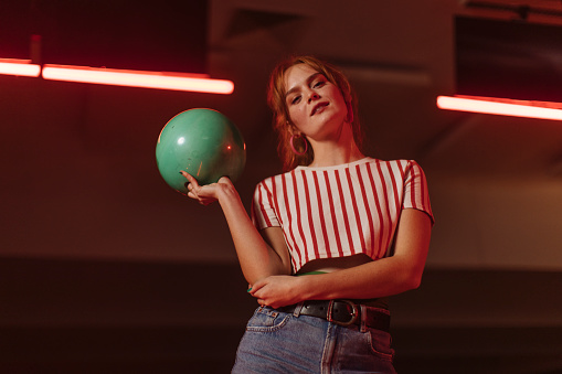 Young redhead woman chooses a bowling ball and prepares for a bowling game