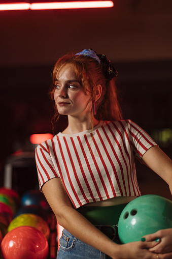 Pretty girl in striped shirt holding bowling ball with both hands