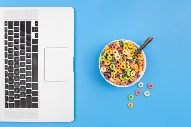 Colored breakfast cereal in a bowl and laptop on a blue background, breakfast and work concept, conceptual minimalism, flat lay.