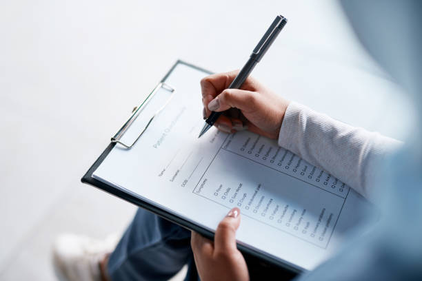Hands, documents and writing with a woman in a hospital, filling out an application or questionnaire for healthcare overhead. Medical, checklist and paperwork with a person filing an insurance report stock photo