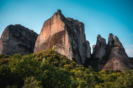 A magnificent view of  world famous rock formations behind the top of a Mediterranean forest. Giant boulders of Meteora framed by blue skies.