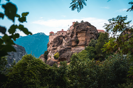 A photo of a hill-shaped boulder and a famous Orthodox monastery on top of it, vast valley in the background. Shot from the forest.