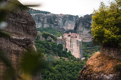 High angle shot of a valley with cliffs all around and a famous monastery on top of a rock formation in the distance.