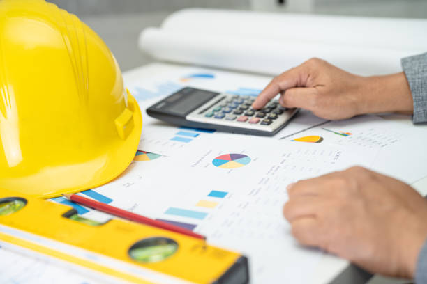 istock Asian engineer with architectural house plan project blueprint, graph and yellow helmet and engineering construction tools. 1468684245