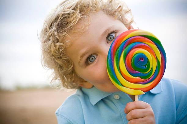 Peek a boo lollipop youth blue eyed boy with blonde curls peeks out from behind a huge colorful lollipop carnival children stock pictures, royalty-free photos & images