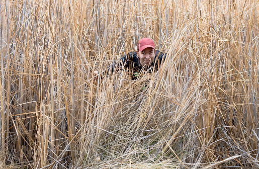 A man sneaks around some tall grass outside in the day time.