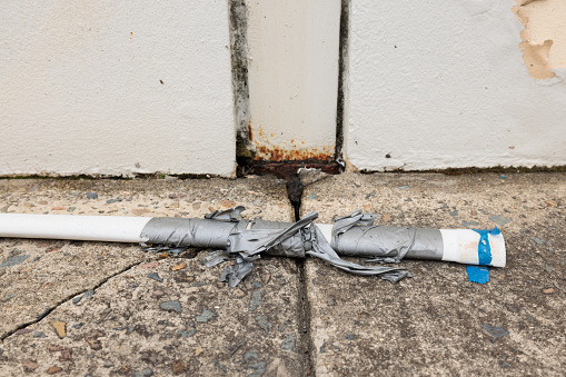 Part of a discarded plastic pipe with electrical tape around it laying on the ground.