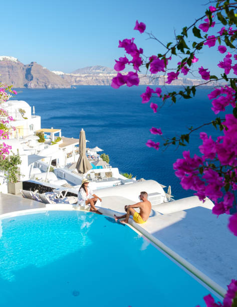 Couple on vacation in Santorini Greece, men and women relaxing by a swimming pool of a luxury resort Couple on vacation in Santorini Greece, men, and women relaxing by a swimming pool of a luxury resort during summer vacation happy couple on vacation in santorini greece stock pictures, royalty-free photos & images