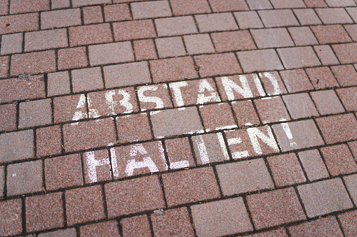 Writing on the sidewalk of a small German town during the Corona Pandemic with the words Abstand halten. Translation: keep your distance