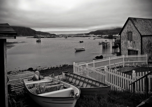 Dark clouds   over a small fishing village with boats and homes in Newfoundland, Canada  in black and white
