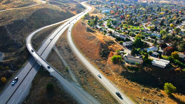 normal speed dolly in drone shot of Highway 1 in Kamloops BC Canada ,  with cars and trucks driving on the road, the city in the background in a desert environment on a sunny day