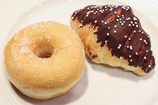 Stock photo showing close-up, elevated view of a plate of pastries containing a glazed ring doughnut and chocolate covered croissant.