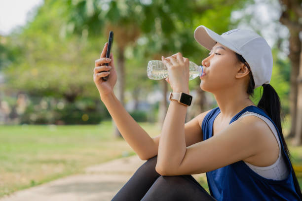istock Young beautiful asian drinking water from bottle and using smartphone, she resting after jogging at green park 1468734069